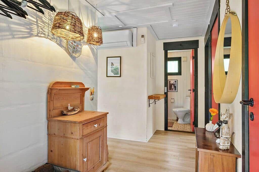 Eingangsbereich mit Holzschrank, Wickerlampen und Blick in die Toilette.