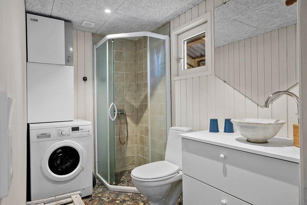 Badezimmer mit Dusche, Toilette, Waschmaschine und Waschtisch mit Schale.