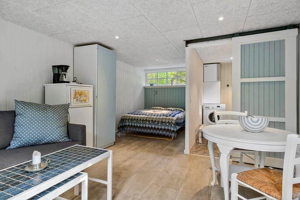 Wohnraum mit Schlafzimmer, Esstisch und Waschmaschine. Holzfußboden und weiße Möbel.