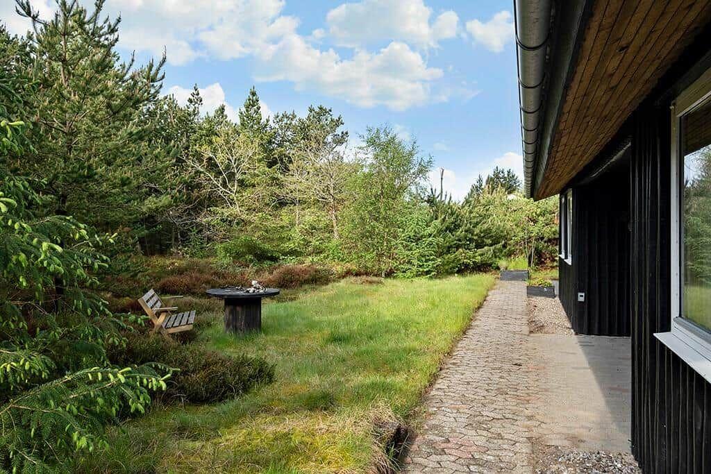 Hinter dem Haus führt ein Kiesweg durch einen grünen Garten mit Bäumen und einem Holztisch.