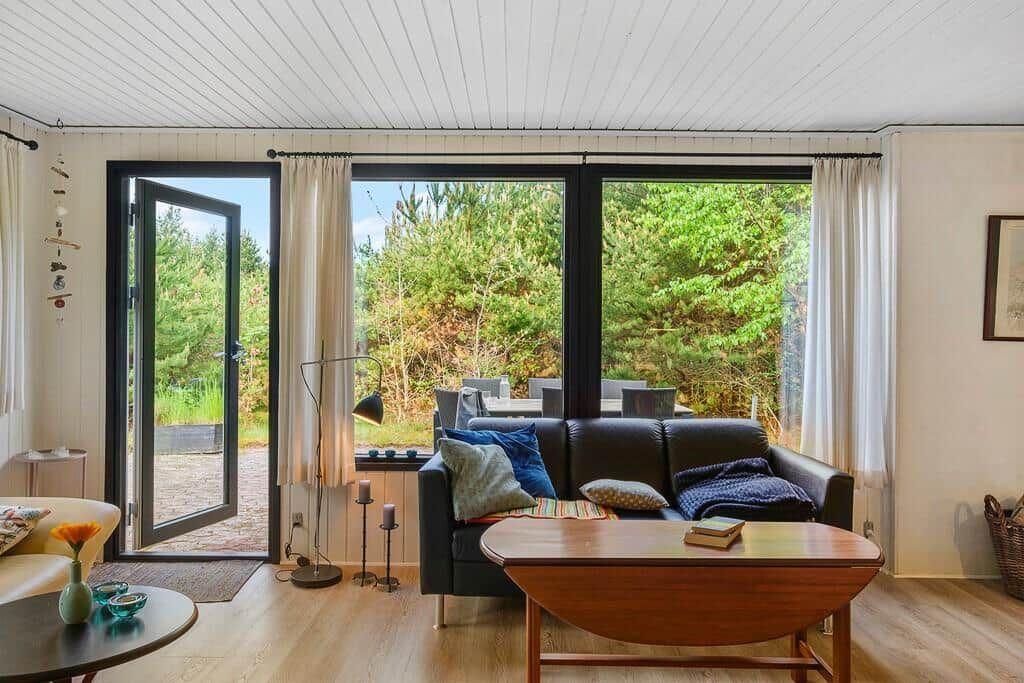 Wohnzimmer mit Sofa, Tisch und Blick auf Garten durch große Fenster.