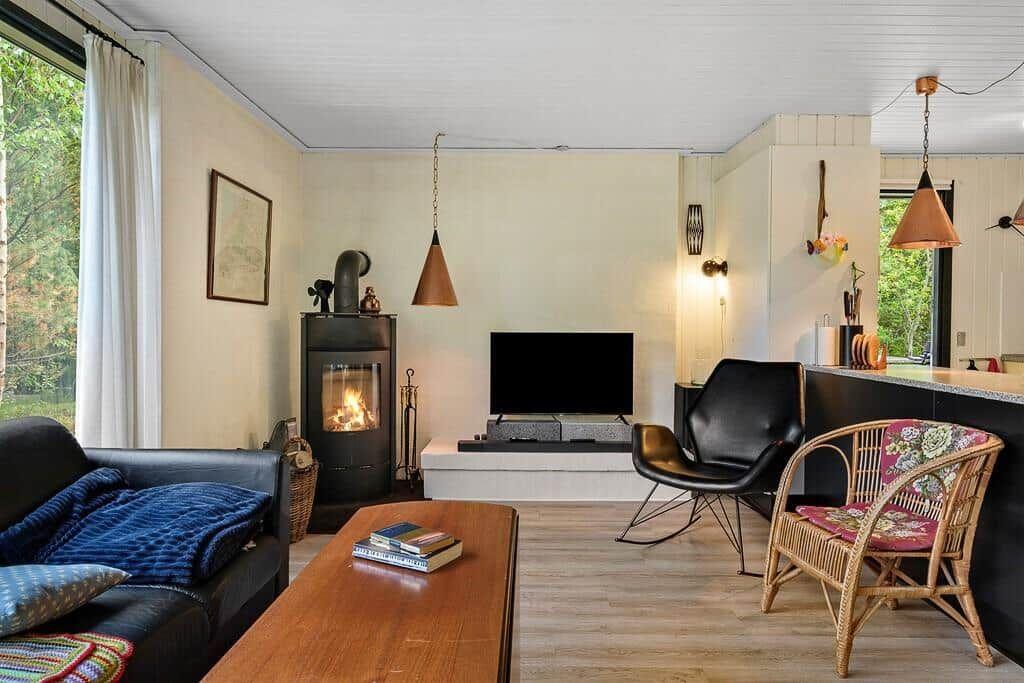 Wohnzimmer mit Kamin, Sofa, Fernseher und Stühlen. Holzboden und große Fenster.