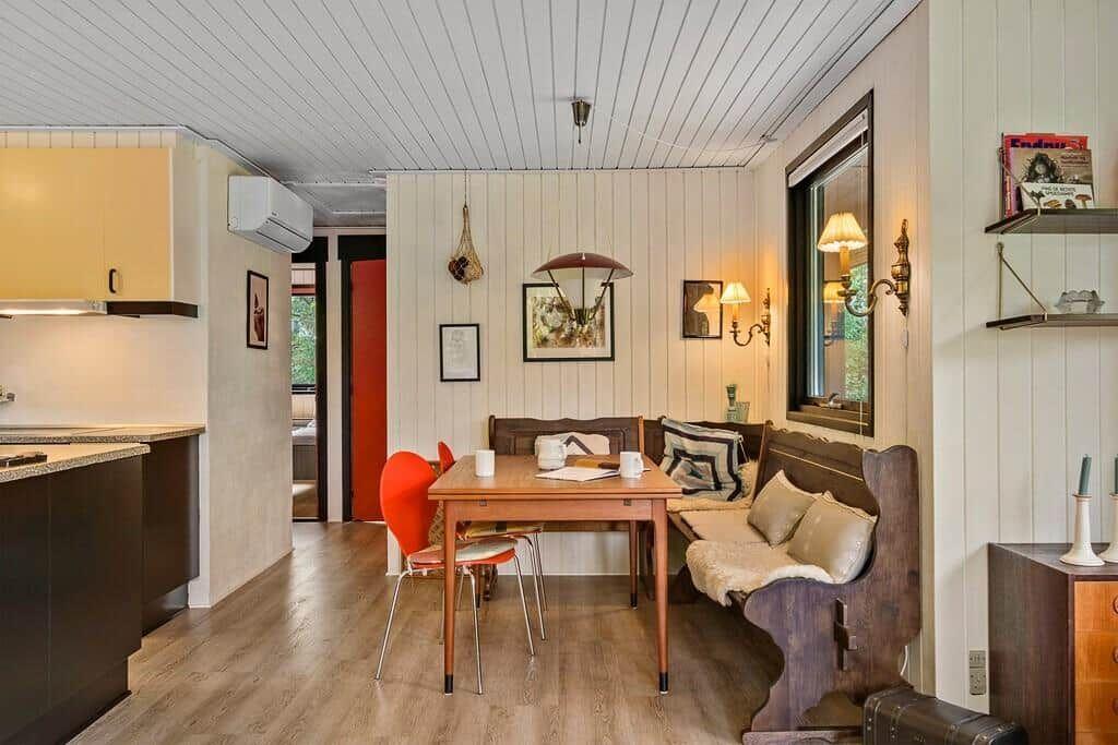Essbereich mit Holztisch, Bank und roter Stuhl. Küche links. Holzwand und Decke.