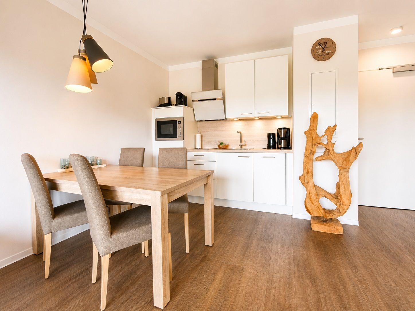 Essbereich mit Tisch und Stühlen. Küche mit weißen Schränken und Holzboden.