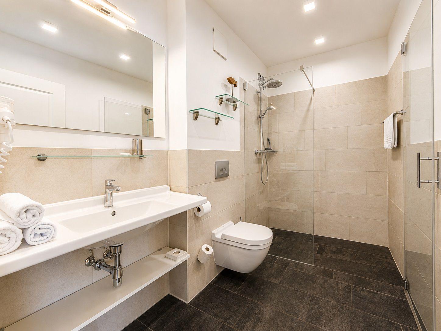 Badezimmer mit Dusche, Waschbecken und Toilette. Fliesenboden und Spiegelschrank.