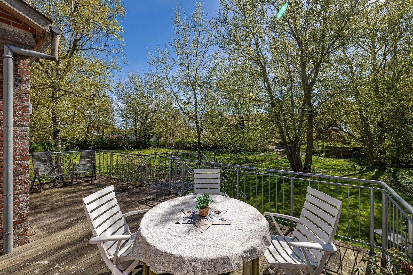 Terrasse mit Tisch und Stühlen, umgeben von Grün und Bäumen.
