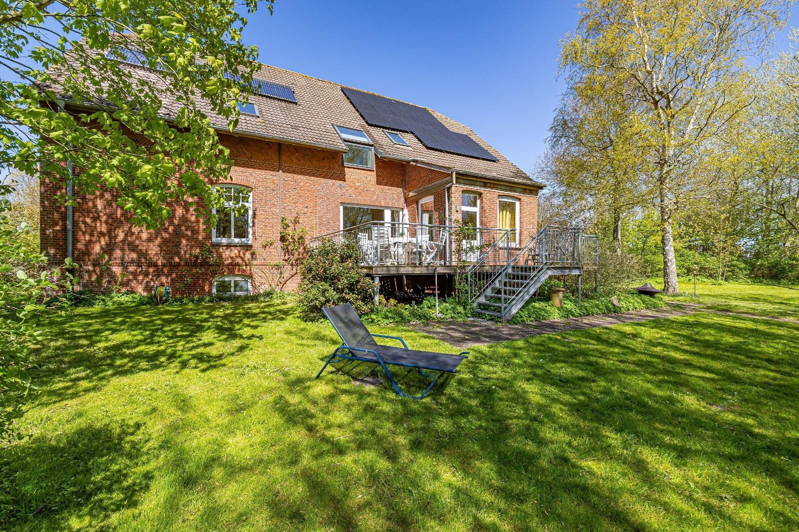 Rotes Backsteingebäude mit Balkon, Sonnenkollektoren und Garten mit Liegestuhl.