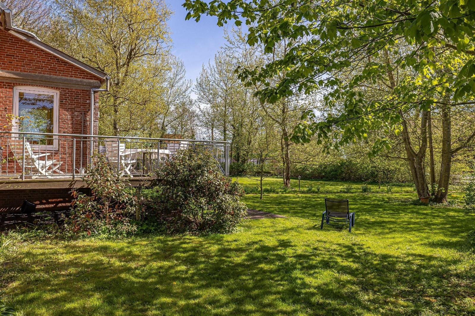 Rotes Backsteingebäude mit Terrasse und Garten. Ein Stuhl steht auf dem Rasen.