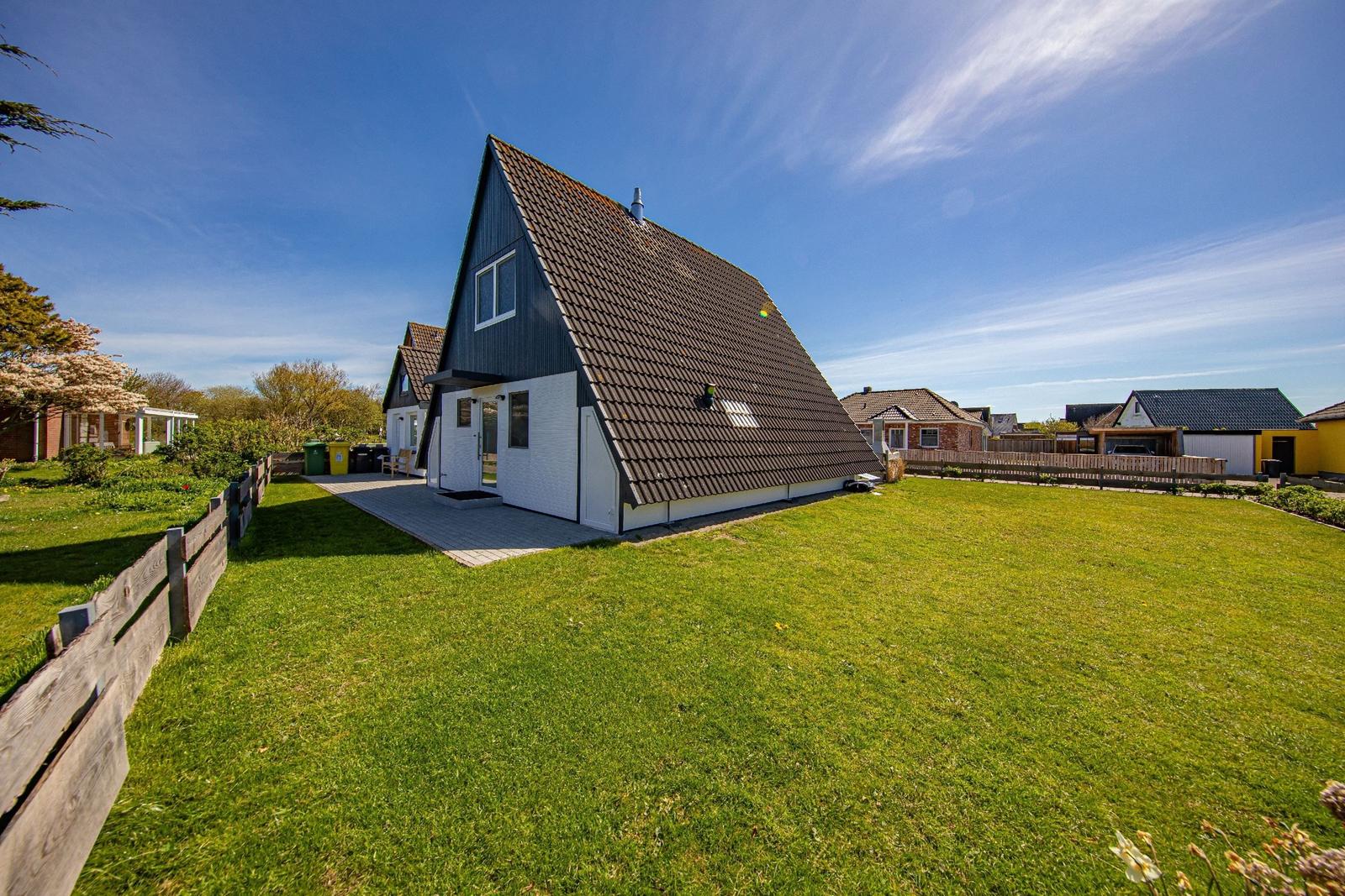 Ein Haus mit schwarzem Dach und weißer Fassade auf grünem Grund.