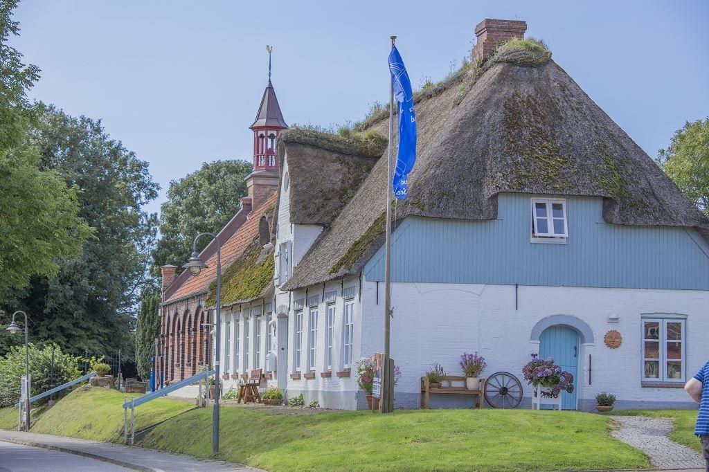 Traditionelles Haus mit Strohdach und blauer Tür. Neben einem Kirchengebäude mit Turm.