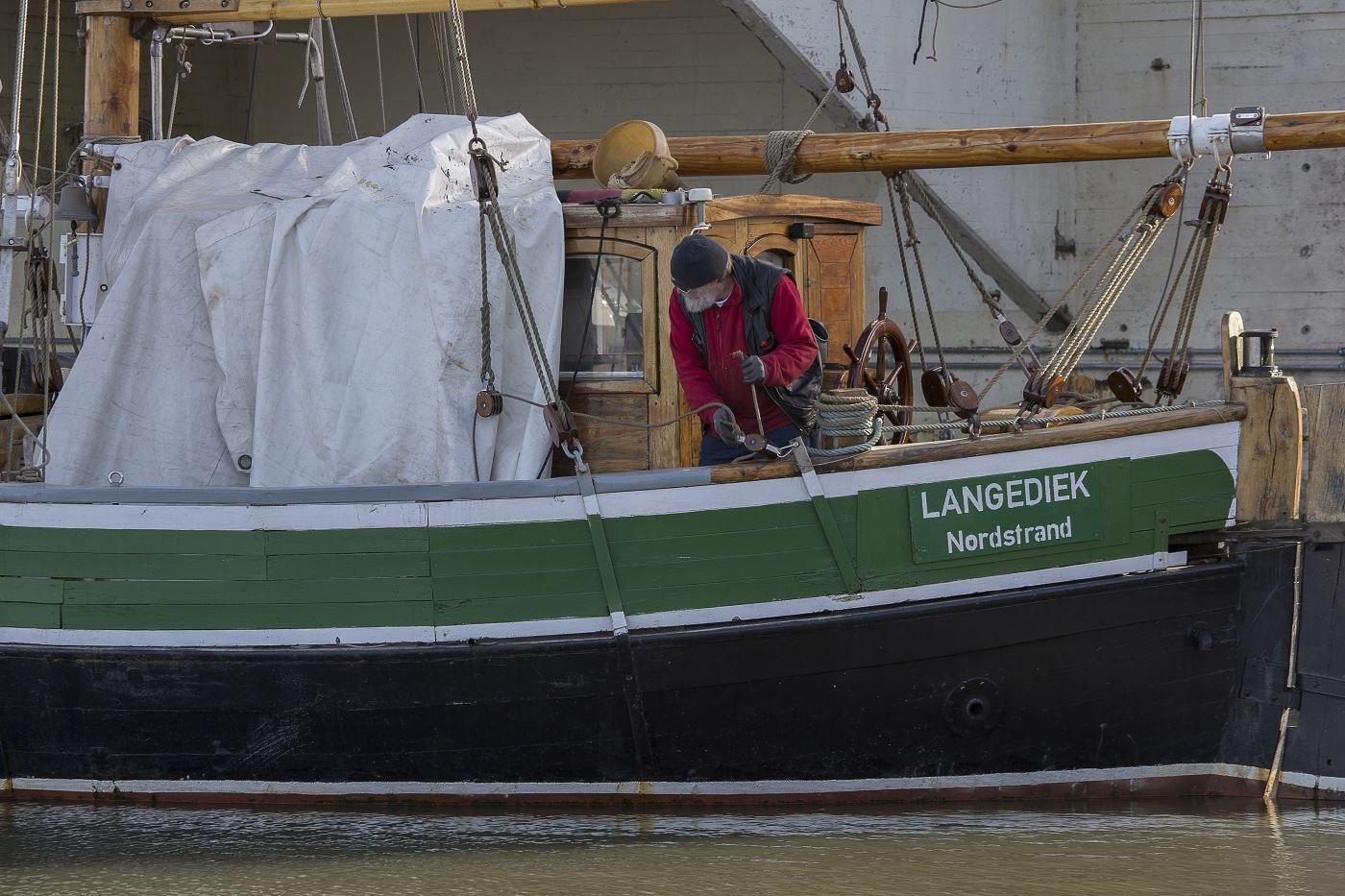 Ein Mann arbeitet an einem traditionellen Schiff mit der Aufschrift LANGEDIEK Nordstrand.