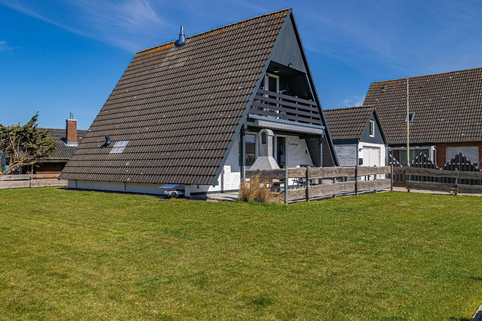 A-Frame-Haus mit Terrasse, Garten und Holzzaun unter blauem Himmel.