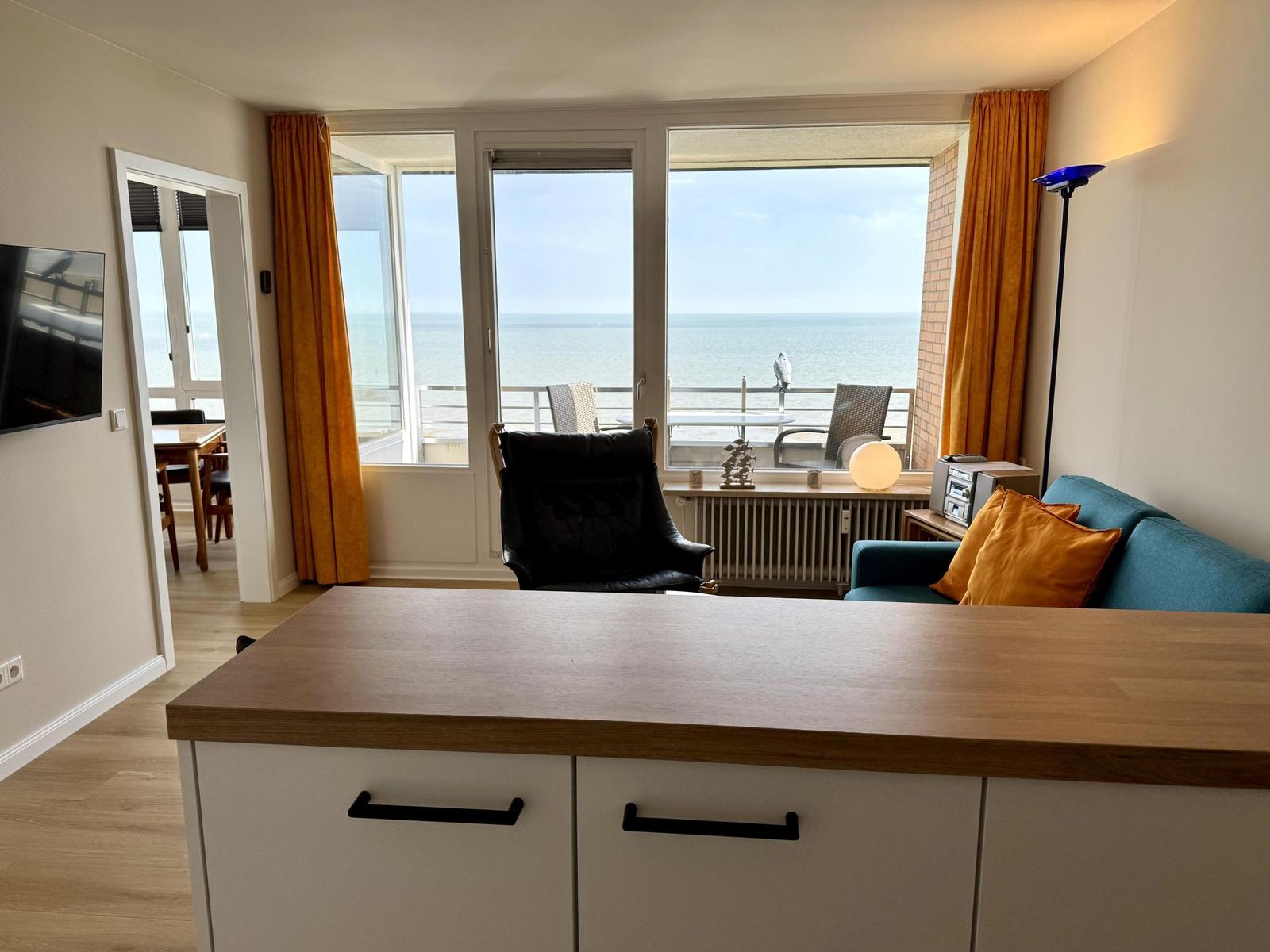 Living room with sea view, sofa, armchair, and kitchen island.