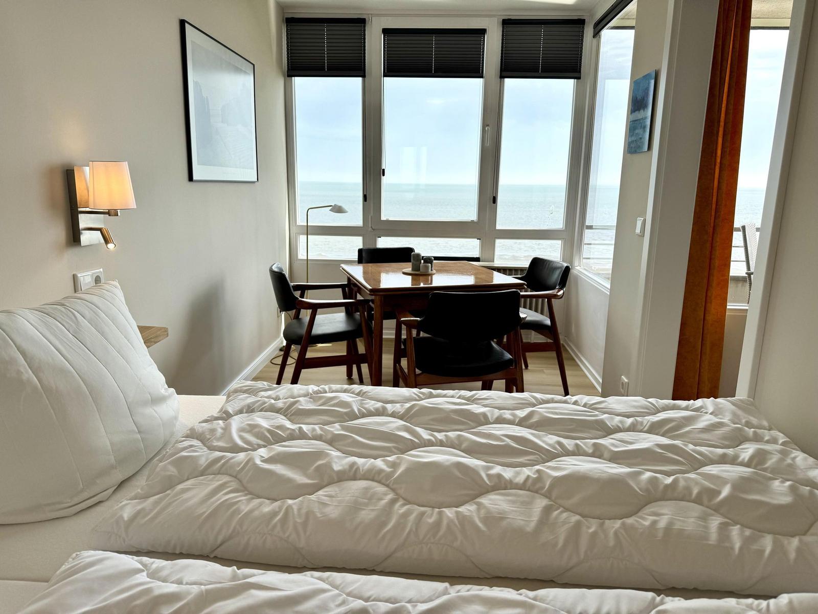 A bedroom with sea view and dining area with table and chairs.