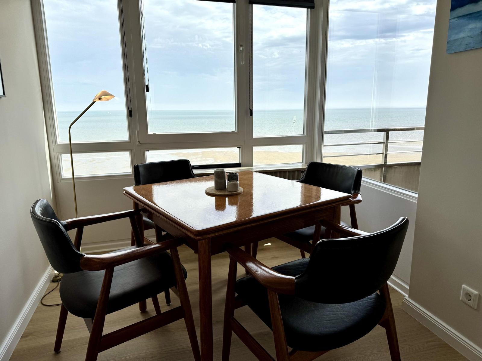 Dining table with four chairs in front of large window with sea view.