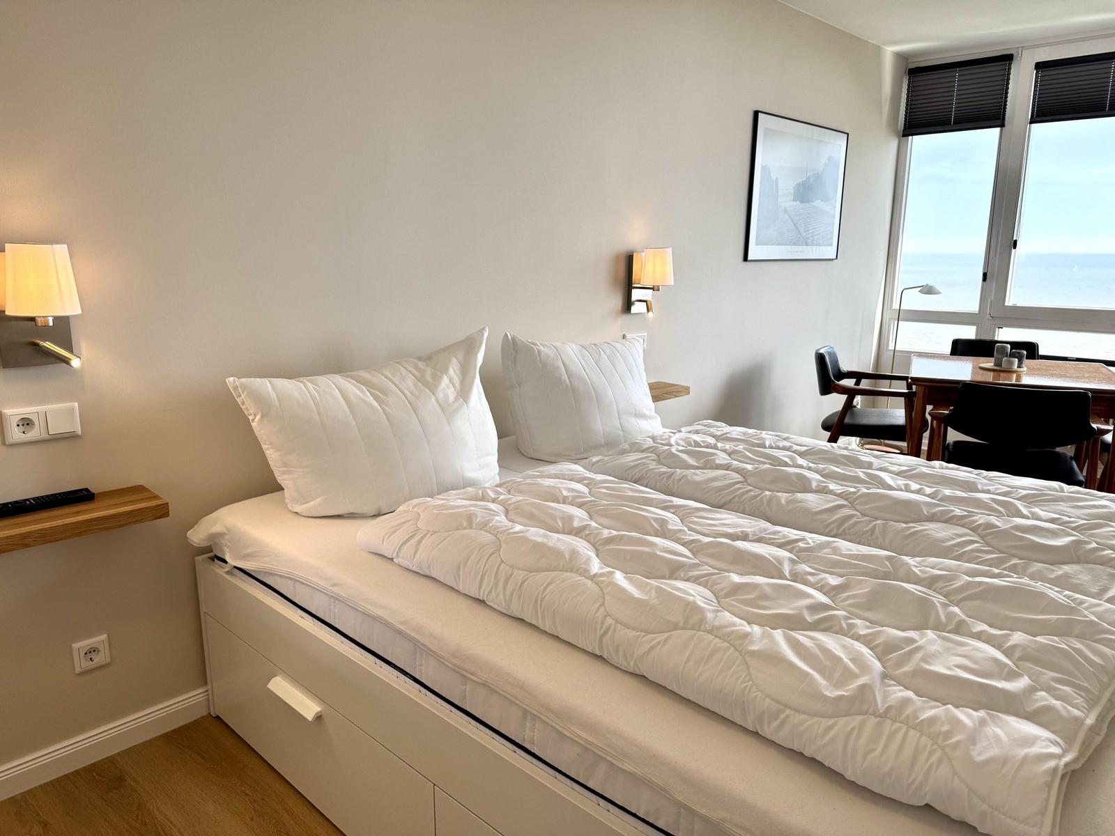 Bedroom with double bed, table and chairs. Window with sea view.