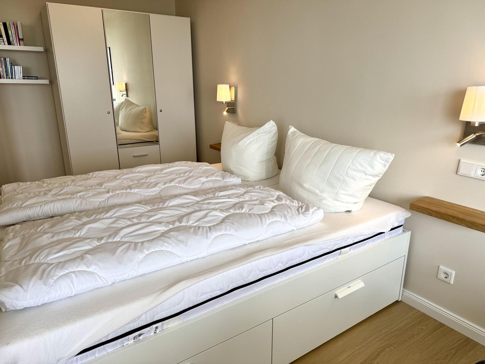 Bedroom with white bed, nightstand, and mirrored wardrobe