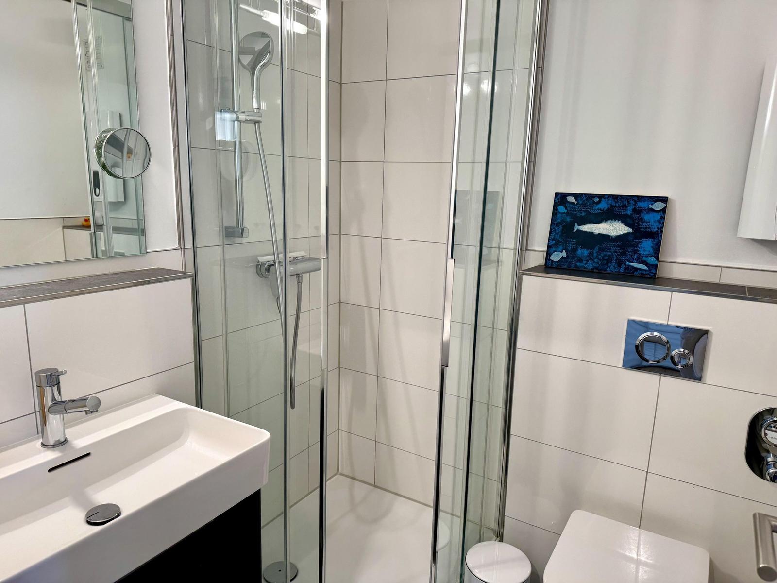 Bathroom with shower, sink, and toilet. Wall art with fish motif.
