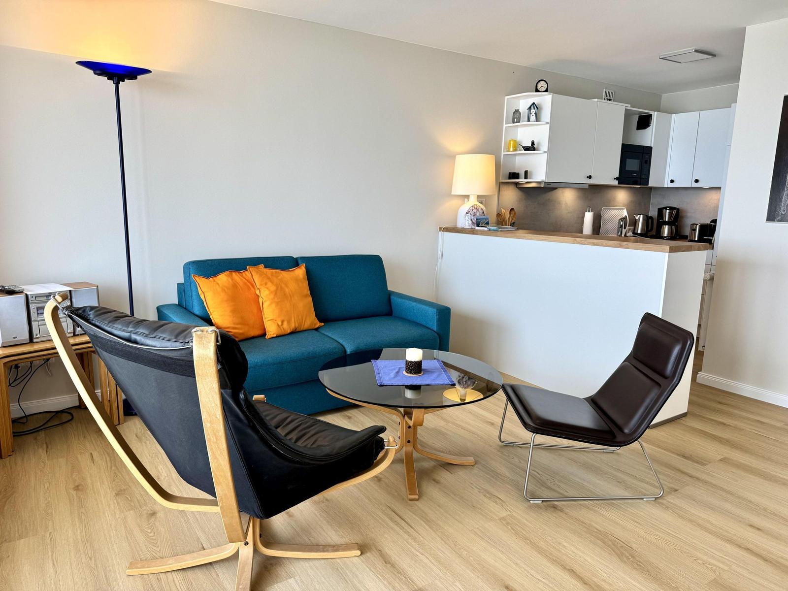 A living area with a blue sofa, two black chairs, and a round table.