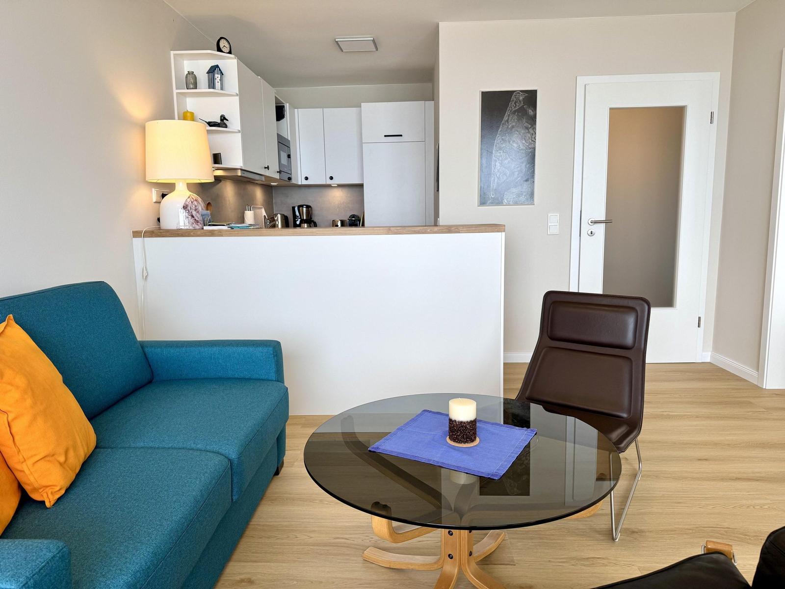 Blue sofa with orange cushions, round glass table, and brown chair in the living area.