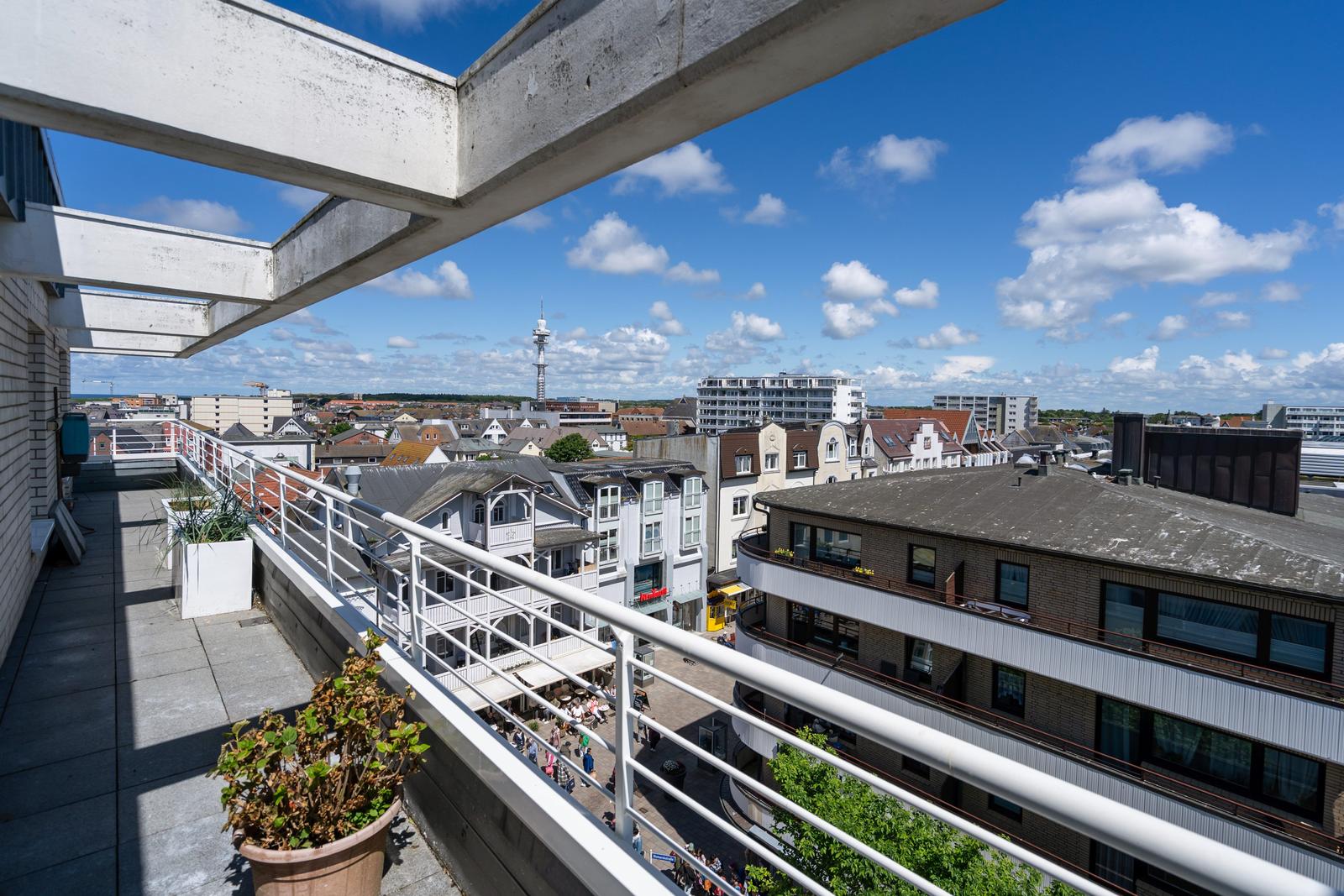 Terrasse mit Blick auf Stadt und Turm unter blauem Himmel mit weißen Wolken.