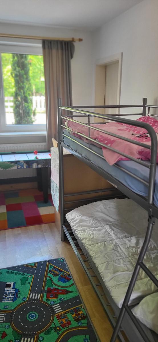 Zimmer mit Doppelstockbett, buntem Teppich und Fenster mit Blick nach draußen.