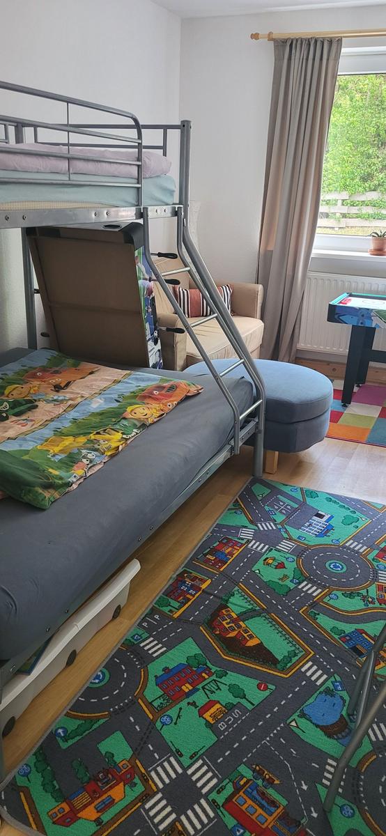 Zimmer mit Doppelstockbett, Spielteppich und Fenster mit Blick auf Garten.