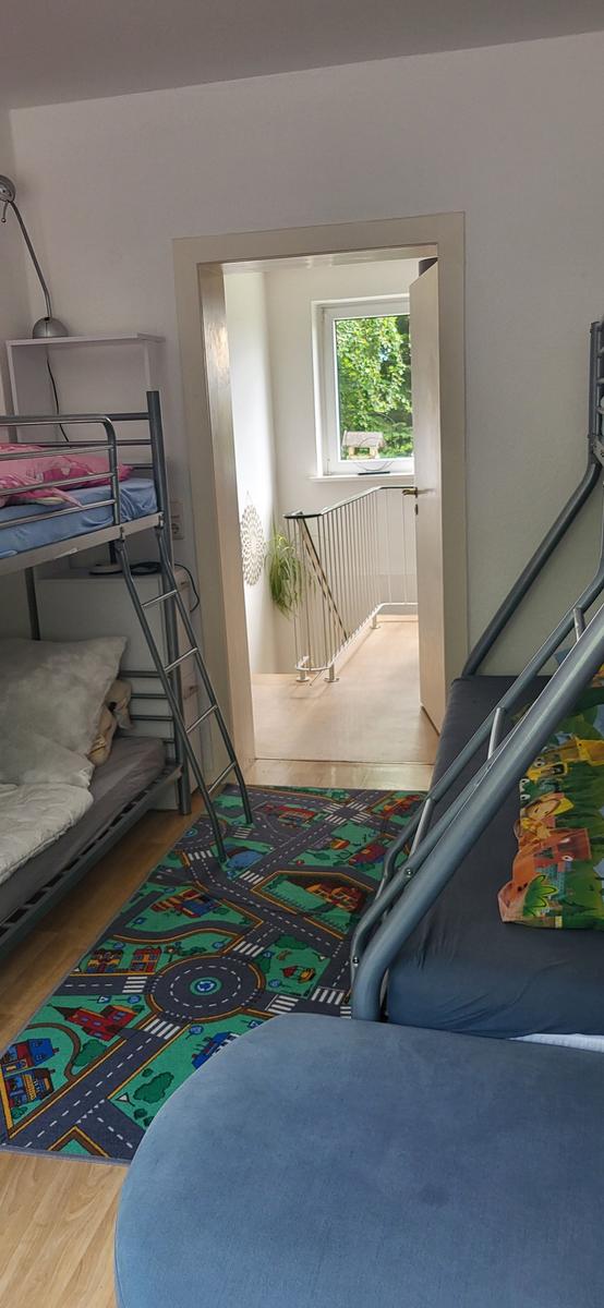 Zimmer mit Doppelstockbetten und Kinderzimmer-Teppich. Durchgang zum Flur mit Fenster.