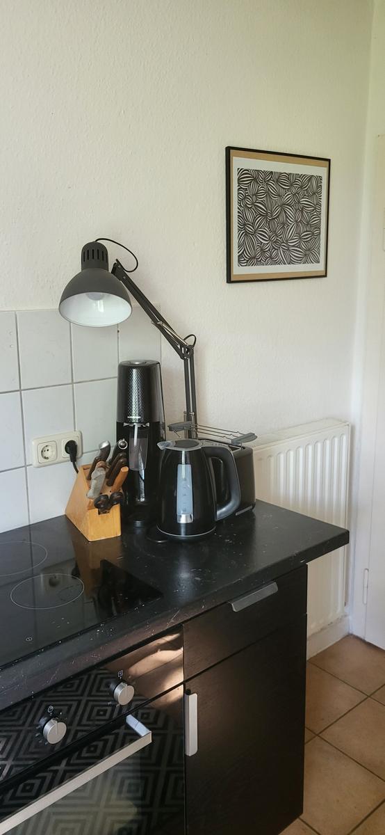 Küchenzeile mit Kochfeld, Kaffeemaschine, Wasserkocher und Stehlampe.