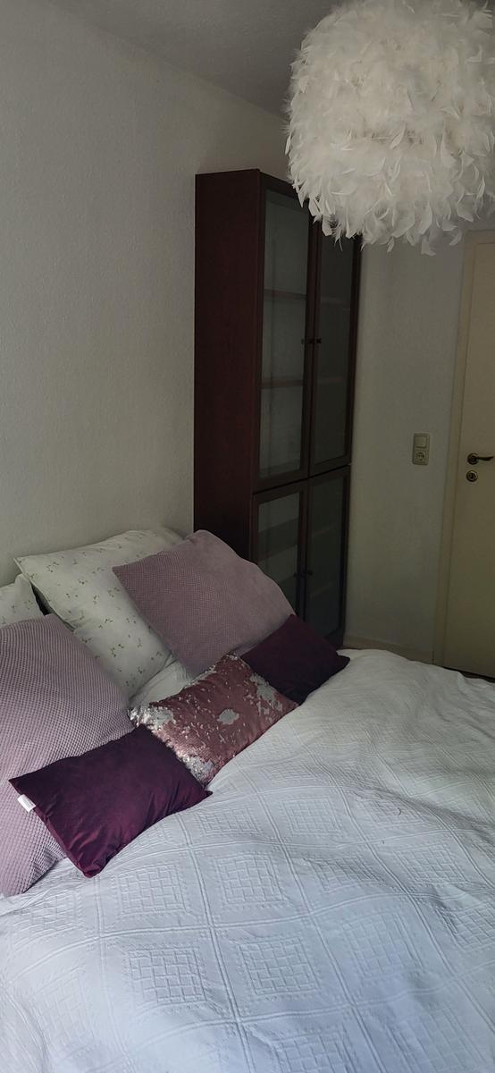 Schlafzimmer mit Bett, Kissen und Glaswand-Schrank. Deckenleuchte mit Federdekoration.
