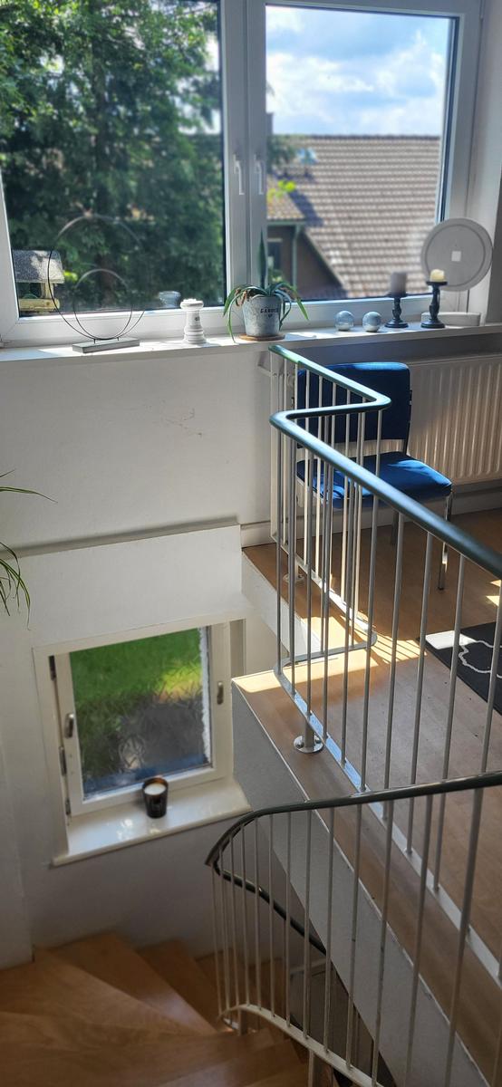 Treppe mit Geländer führt zu einem Raum mit großem Fenster und Blick auf Grün.