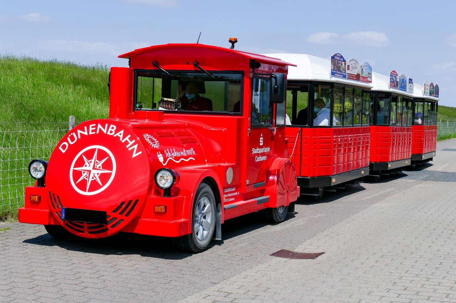 Roter Dünenschienenbus mit mehreren Wagen steht auf einem gepflasterten Weg.