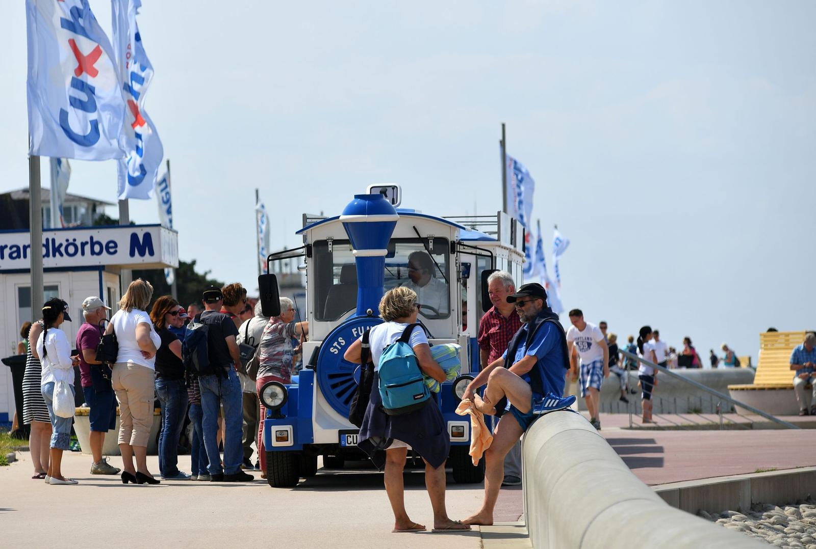 Besucher warten an einer Strandbahnstation. Ein blauer Zug steht bereit.