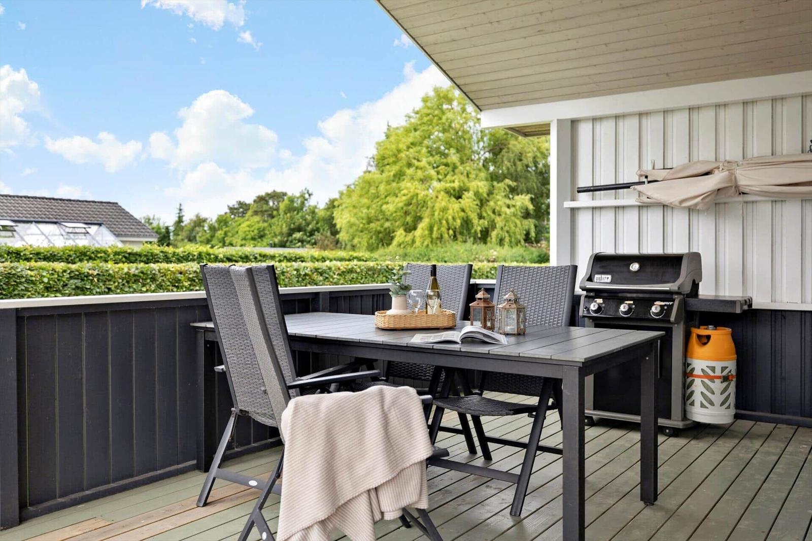 Deck with table, chairs, grill, and view of green areas.