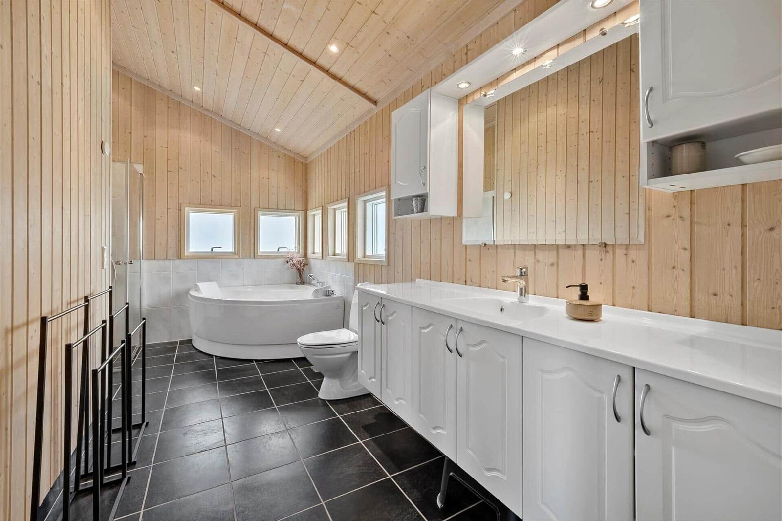 Bathroom with bathtub, toilet, and sink. Wooden walls and dark floor.