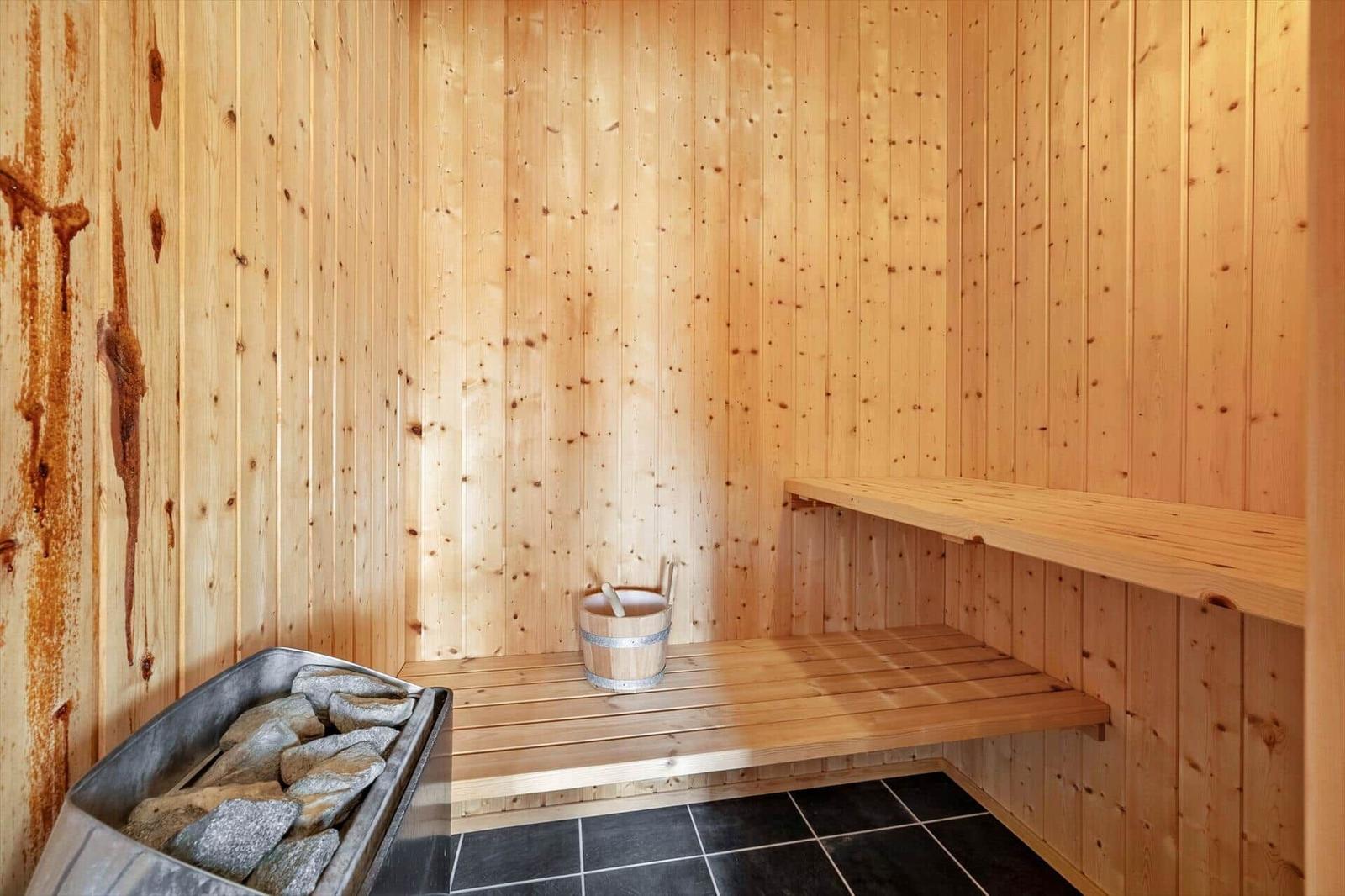 Sauna with wooden walls, bench, and stone tray with bucket.