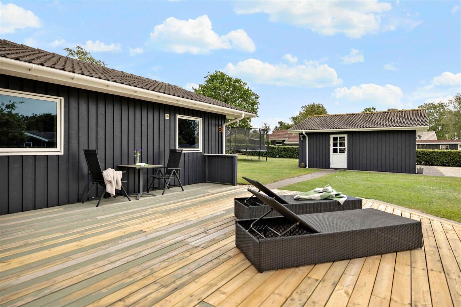 Deck with loungers and table in front of a house with dark cladding.