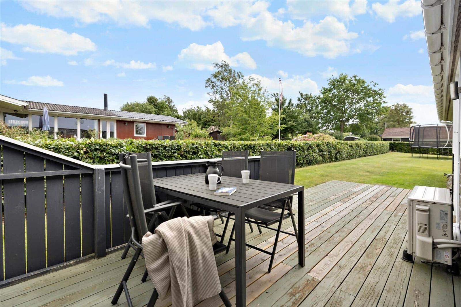 Deck with table and chairs, view of garden and hedge.