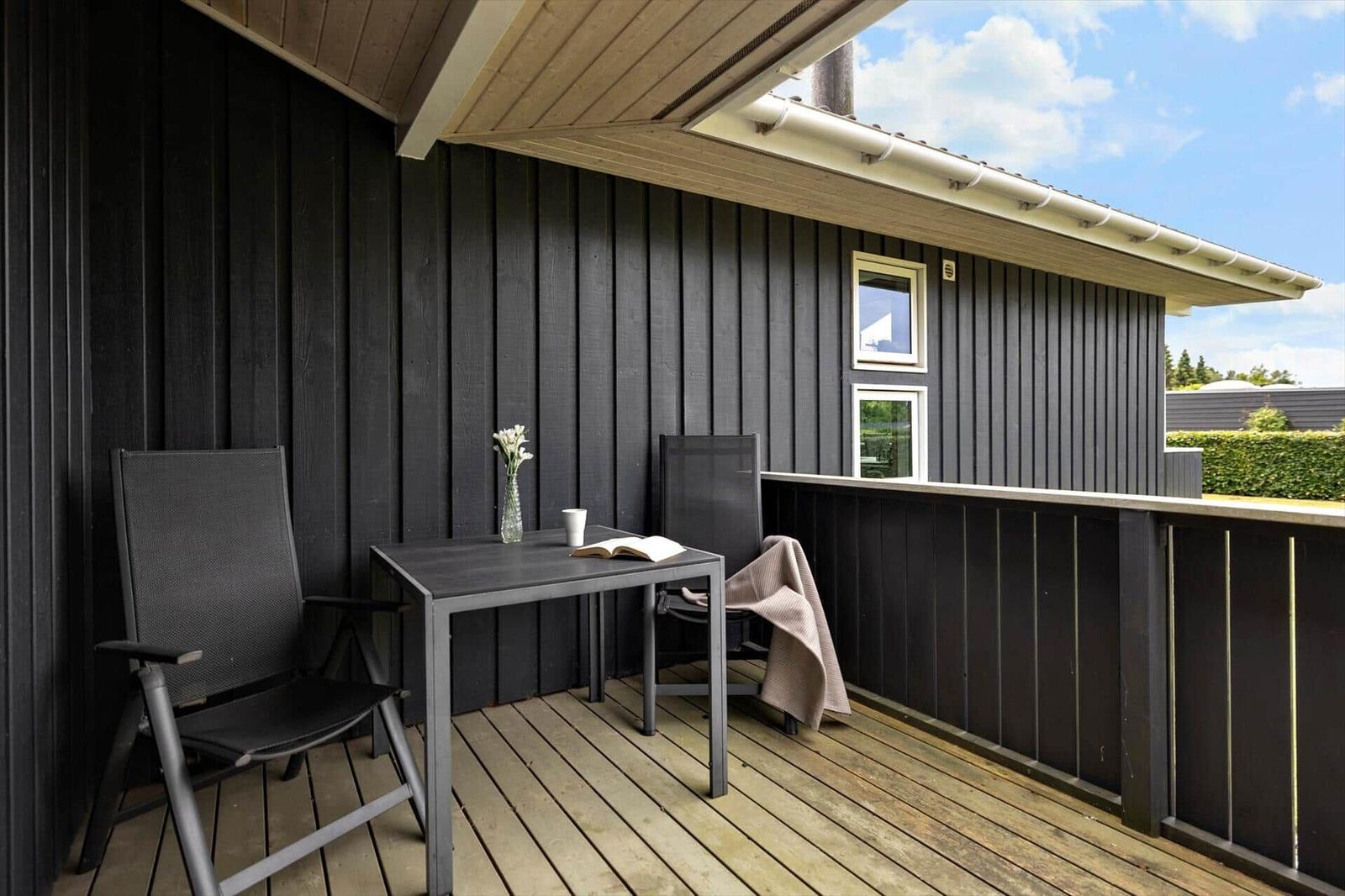 Deck with table, two chairs, flowers, and view of green areas.