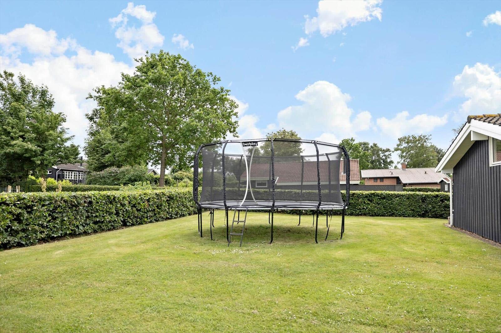 A black trampoline with net stands on a green lawn.