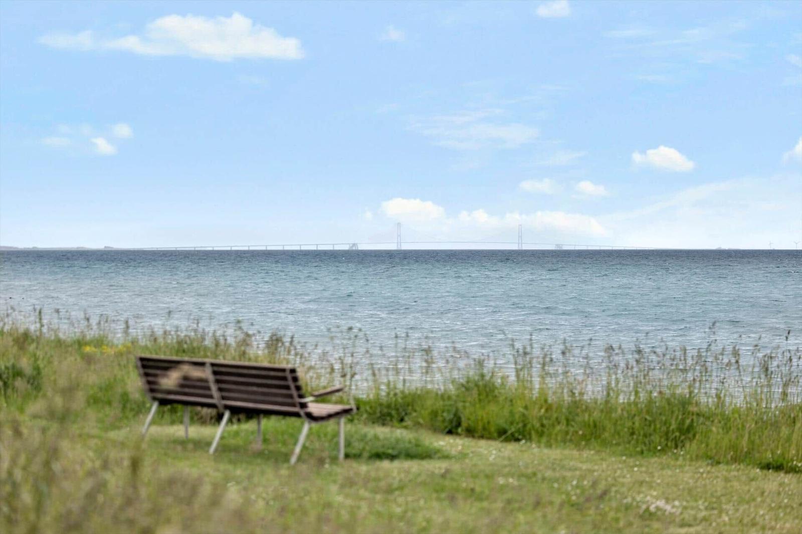 A bench by the shore with a view of a bridge over the sea.
