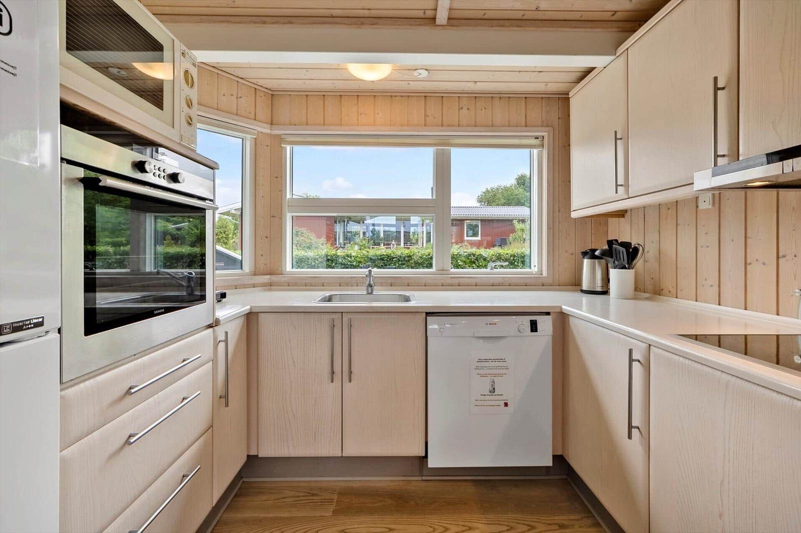 Kitchen with wooden walls, window, sink, dishwasher, and kitchen appliances.