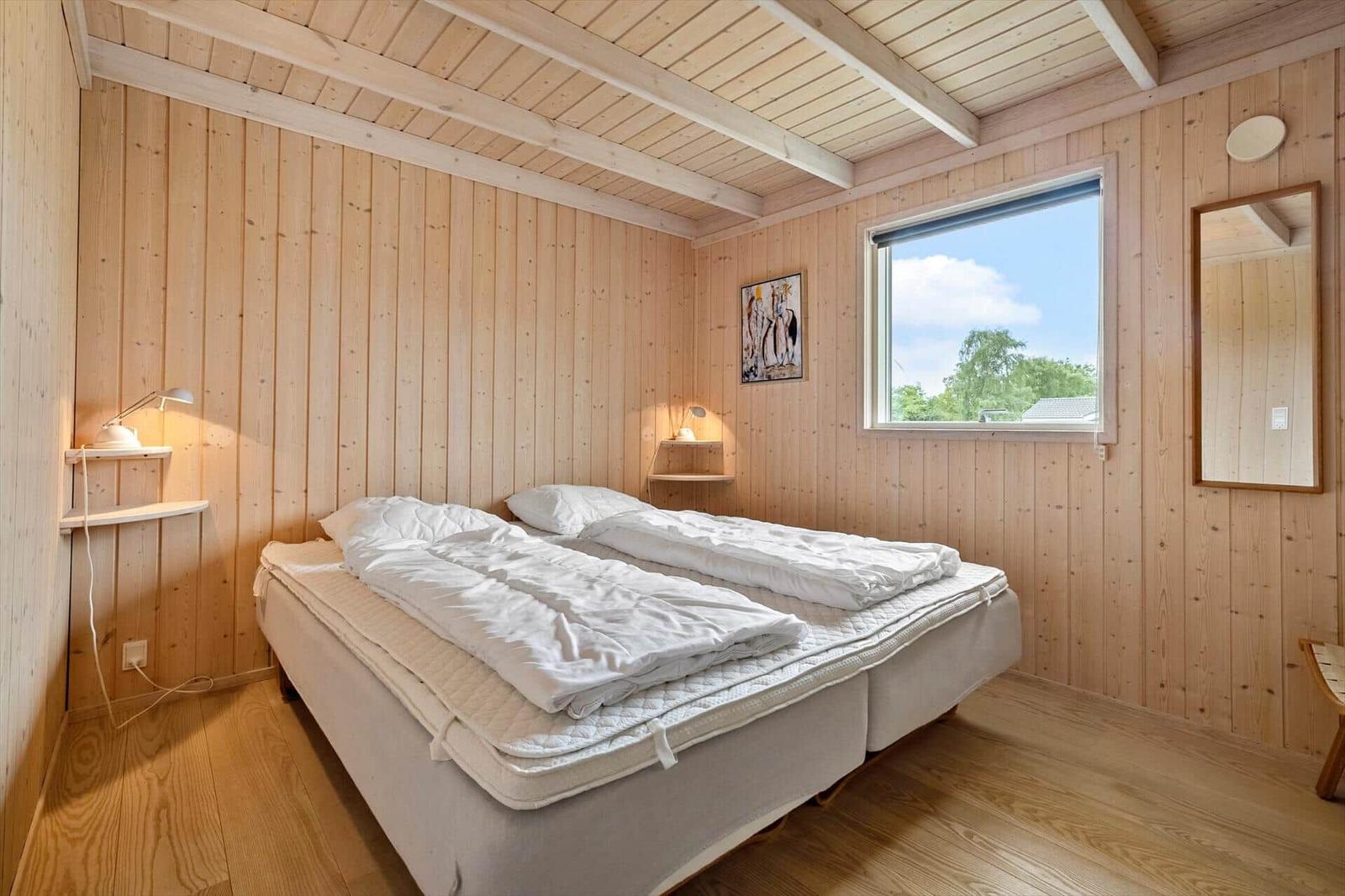 Bedroom with wooden walls, bed, window, and mirror.