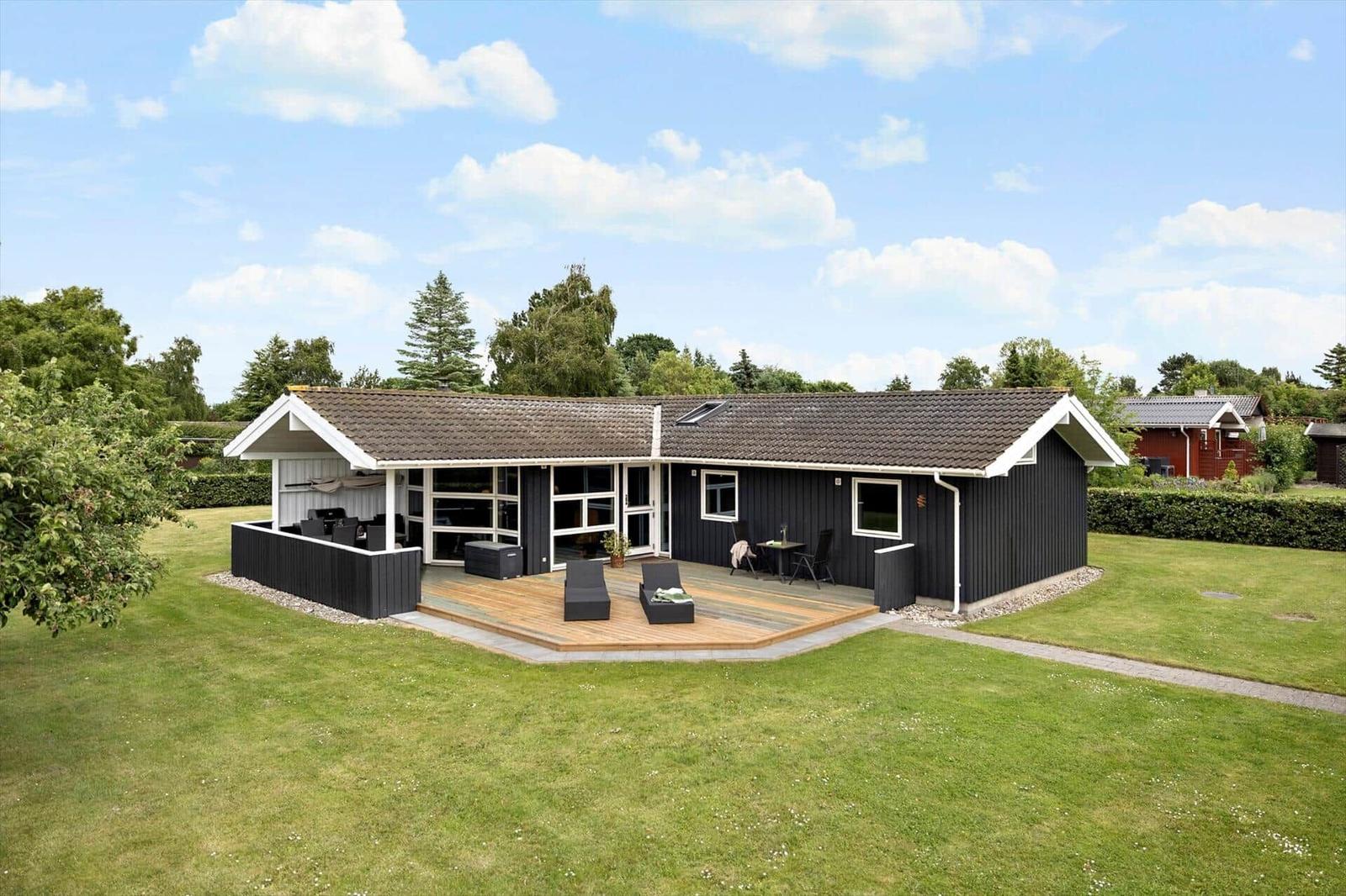 Black house with wooden terrace and garden. Outdoor area with seating.