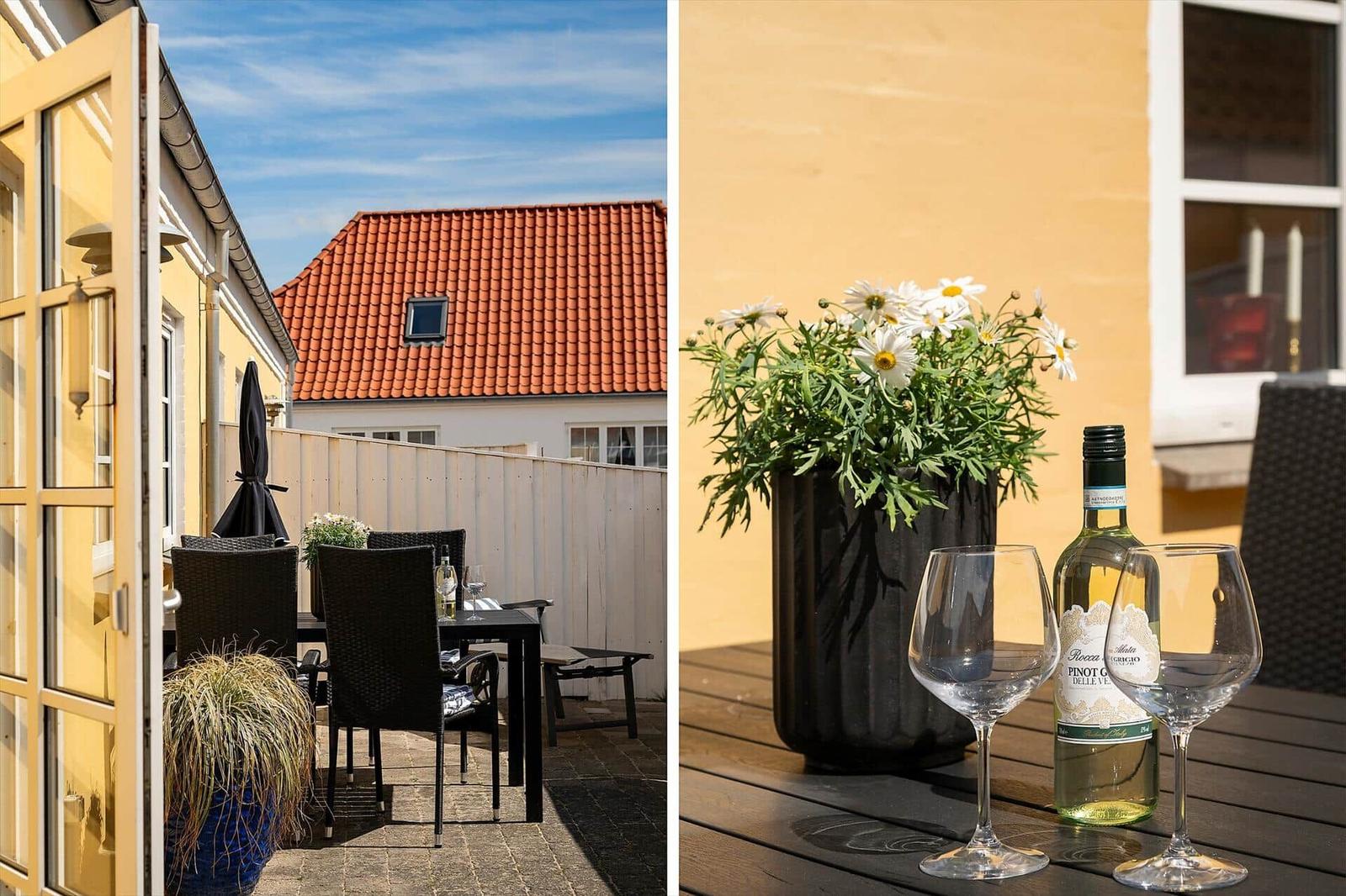 Terrasse mit Tisch, Stühlen und Blumen. Flasche Wein und zwei Gläser auf Tisch.