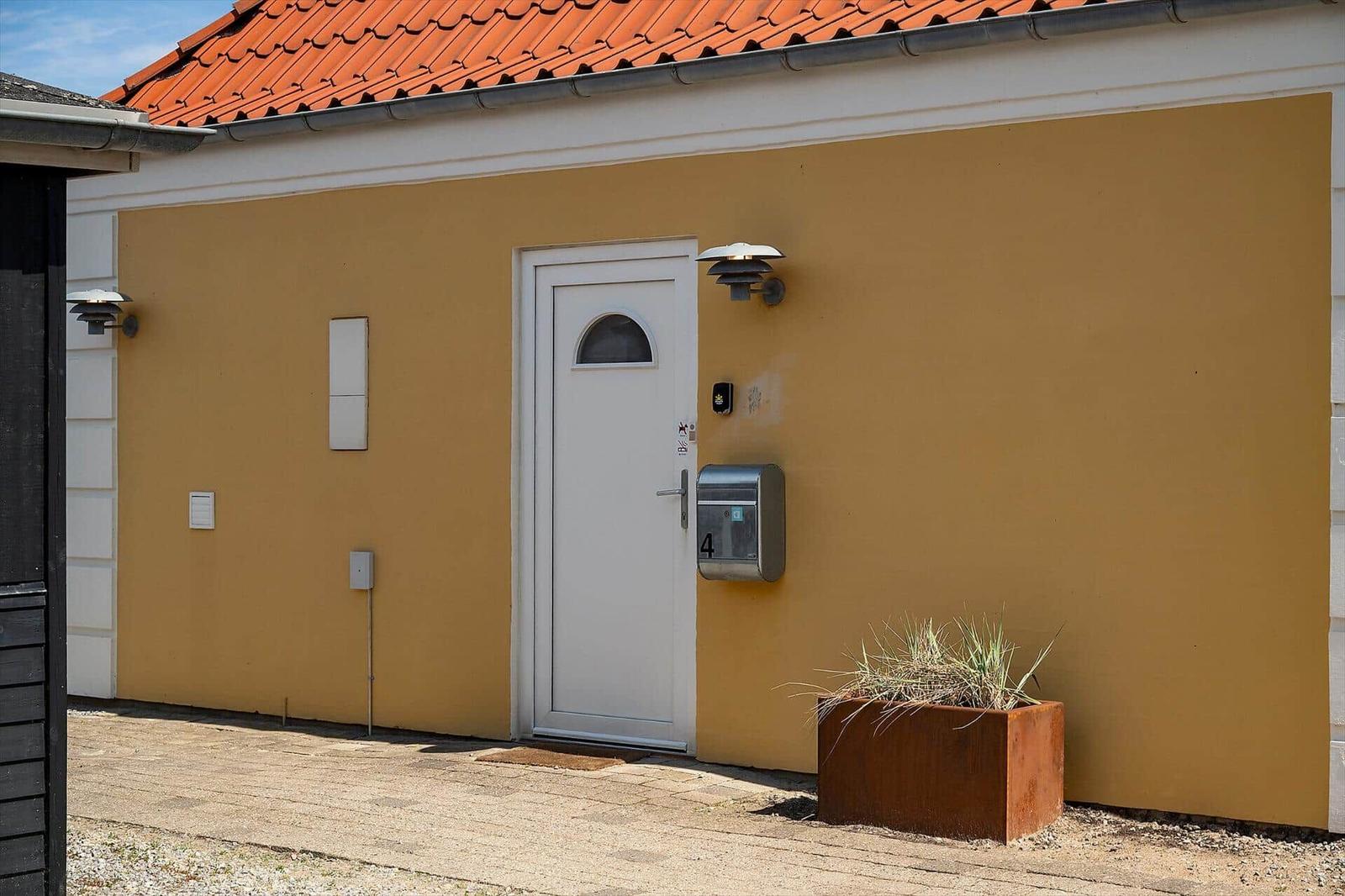 Haus mit gelber Wand, weißer Tür und rotem Ziegeldach. Vor der Tür steht ein Metallbriefkasten.