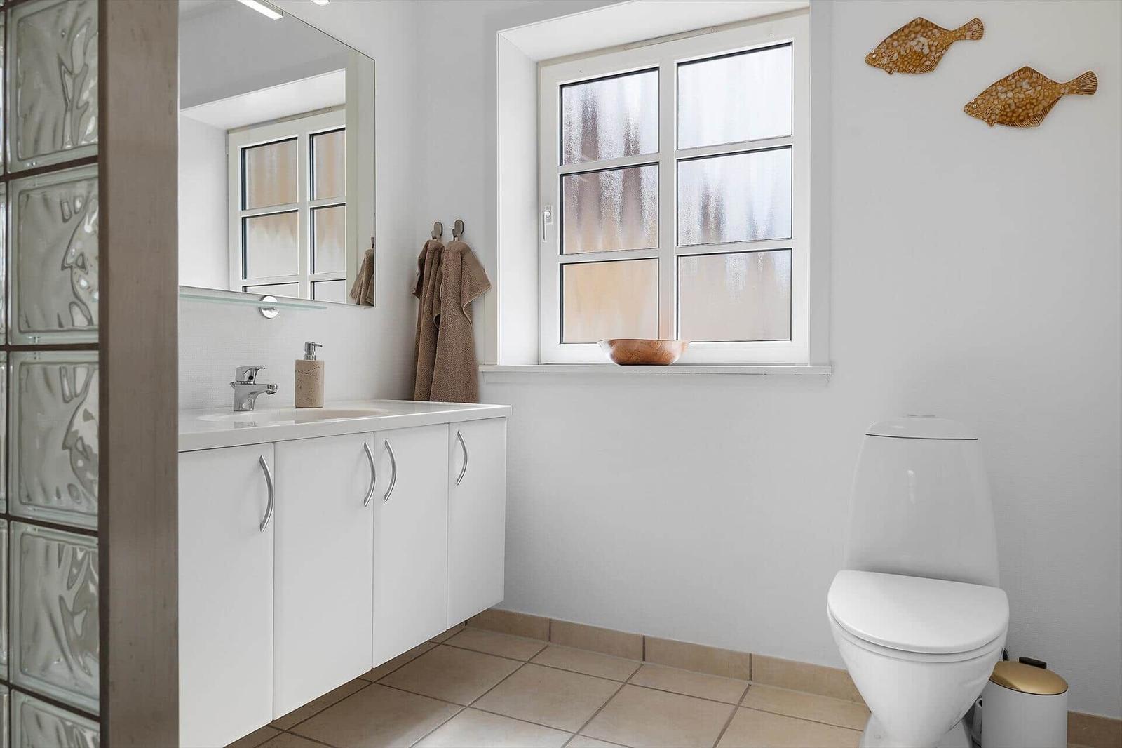 Badezimmer mit Waschbecken, Toilette und Fenster mit getöntem Glas.