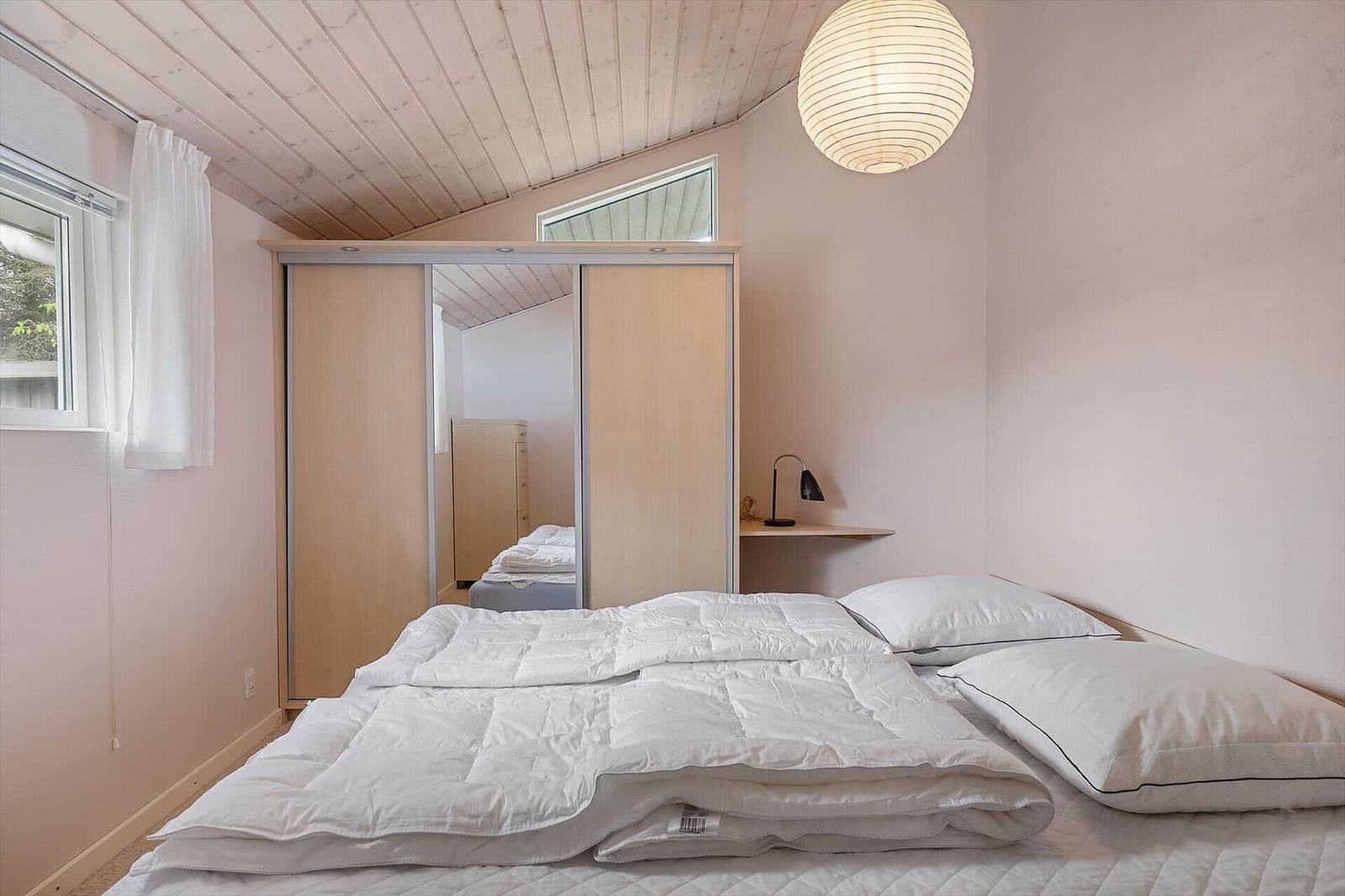 Schlafzimmer mit Bett, Schrank und Fenster. Decke aus Holz, Lampe und Nachttisch.