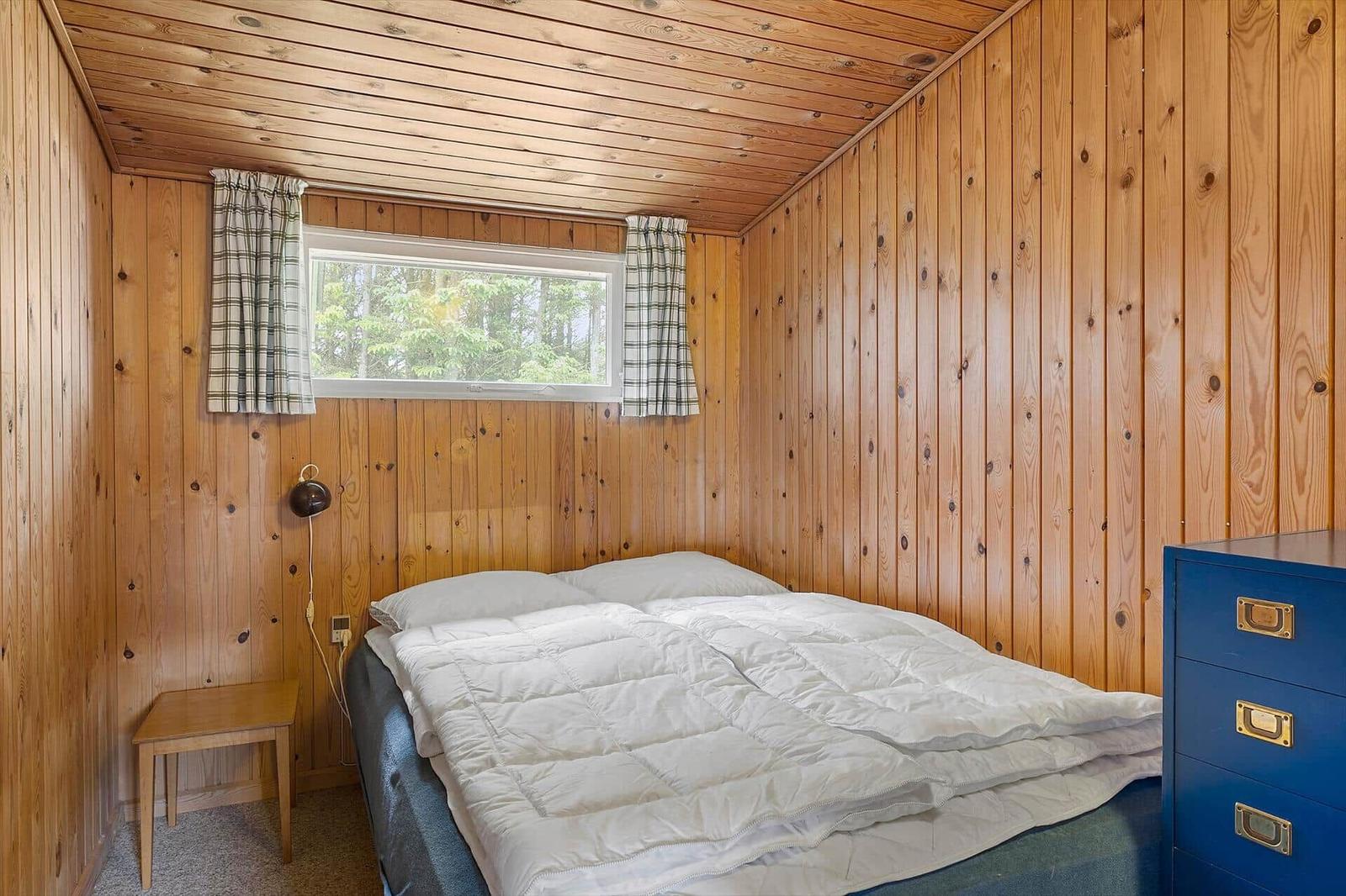 Schlafzimmer mit Holzwand, Bett, Fenster und blauem Schrank.