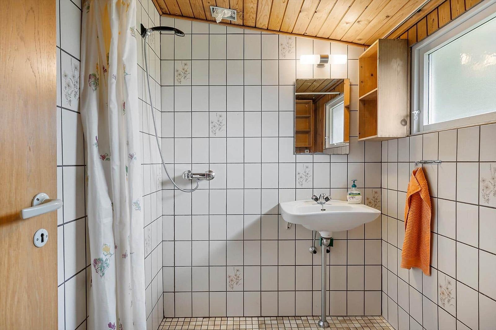 Badezimmer mit Dusche, Waschbecken und Holzregal an der Wand.